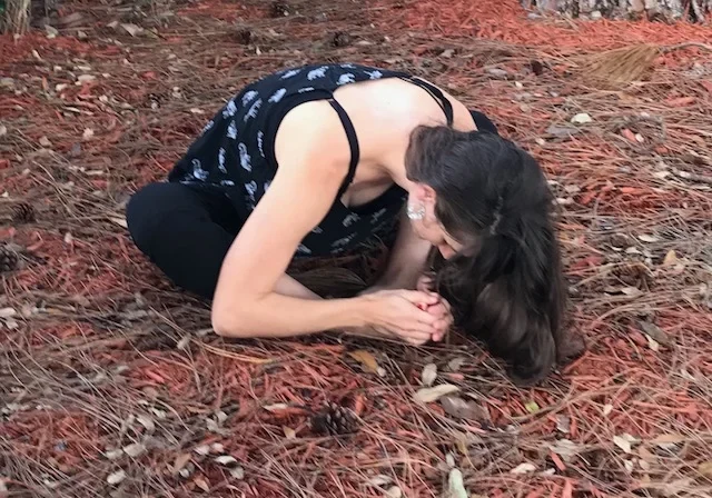 Angela practicing yoga outdoors among pine needles